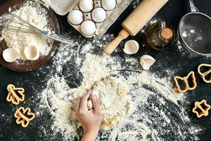 kvinnas händer knåda deg på tabell med mjöl, ägg och Ingredienser. topp se. foto