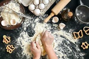 kvinnas händer knåda deg på tabell med mjöl, ägg och Ingredienser. topp se. foto