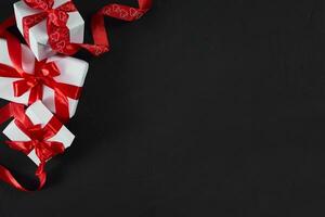 vit gåva lådor med röd band på svart bakgrund. valentines dag hälsning kort. foto