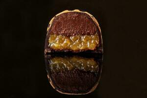 skära lyx handgjort godis med choklad och gul confiture fyllning på svart bakgrund. foto