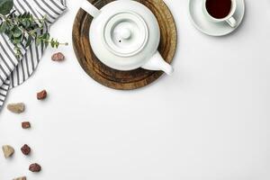 en vit porslin tekanna på en trä- styrelse och en vit kopp med te på en tabell. topp se. kopia Plats. foto