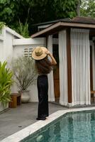 skön modell kvinna i trendig solglasögon och svart sommar utrusta med sugrör hatt Framställ på modern villa. full längd. foto