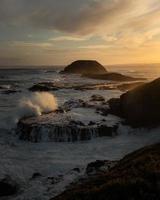 vatten i grovt hav krossade mot klipporna i Australien vid solnedgången foto