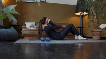 ung kvinna som ligger på yogamatta och gör sit ups i vardagsrummet foto