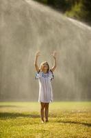 söt liten flicka som har kul under bevattningssprinkler foto