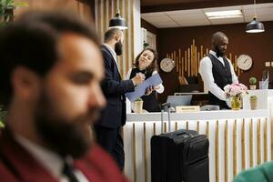 hotell receptionist håller på med kolla upp i för affärsman på främre skrivbord, tillhandahålla lyx concierge tjänster till gäst. klient signering papper och reser för arbete företag möten utomlands. foto