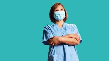 livlig sjukvård specialist bär skyddande medicinsk ansikte mask till sluta virus spridning. stänga upp av Lycklig leende sjuksköterska i professionell enhetlig med vapen vikta, isolerat över studio bakgrund foto