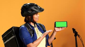 bipoc kvinna innehav krom nyckel grön skärm telefon, som visar tummen upp hand rörelse. leverans cykel ryttare presenter falsk upp pekskärm av smartphone i landskap läge, stänga upp foto