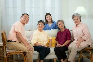 Lycklig asiatisk senior familj och ung kvinna sjuksköterska Sammanträde på soffa i levande rum på Hem foto