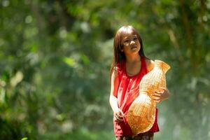 liten asiatisk flicka i röd klänning innehav fiske Utrustning i de skog, lantlig thailand levande liv begrepp foto