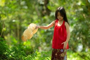 liten asiatisk flicka i röd klänning innehav fiske Utrustning i de skog, lantlig thailand levande liv begrepp foto