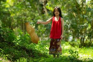 liten asiatisk flicka i röd klänning innehav fiske Utrustning i de skog, lantlig thailand levande liv begrepp foto