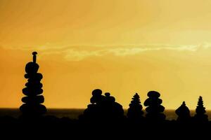 en grupp av staplade stenar i främre av ett orange himmel foto