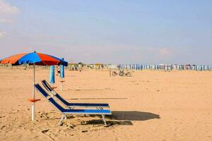 två strand stolar och ett paraply på de sand foto