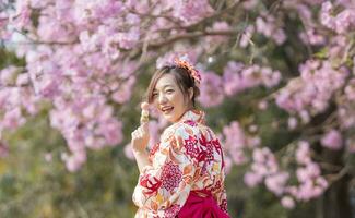 japansk kvinna i traditionell kimono klänning innehav ljuv hanami dango efterrätt medan gående i de parkera på körsbär blomma träd under vår sakura festival med kopia Plats foto