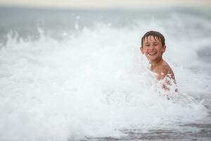 Lycklig pojke åtnjuter hav vågor och vatten stänk.barn förbi de hav. foto