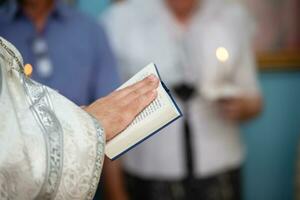 de händer av ett ortodox präst i en kaftan håll en bibeln. foto