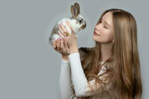 Lycklig ung flicka innehav en vit kanin på en grå bakgrund foto