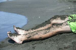 de barnets fötter är täckt med terapeutisk svart magnetisk sand. foto