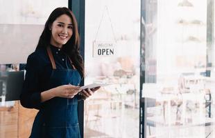 porträtt av en leende asiatisk entreprenör som står bakom sitt café foto