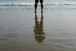 asiatisk mannens fötter och ben på de sandig strand med naturlig solljus i sommar hav foto