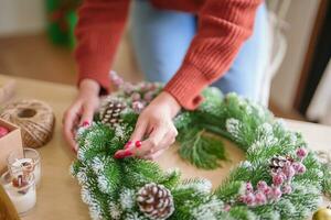 kvinna framställning mistel krans jul krans dekoration med hand tillverkad diy vinter- grönska blomsterhandlare händer framställning jul krans skön mistel. foto