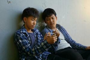 två ung asiatisk Pojkar i hemlighet sat ner kom till rök i en dold hörn av de skola. detta är de beteende av upptäckt en lösning för tonåringar vem ha problem i deras liv förbi använder sig av ämnen. foto