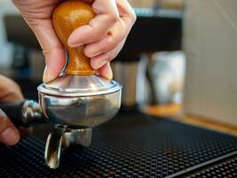 närbild av hand Barista framställning kaffe med manuell trycker på jord kaffe använder sig av manipulera på de trä- disken bar på de kaffe affär foto