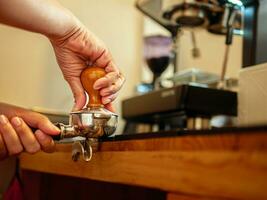 hand av en Barista innehav en portafilter och en kaffe manipulera framställning ett espresso kaffe. Barista trycker på jord kaffe använder sig av en manipulera i en kaffe affär foto