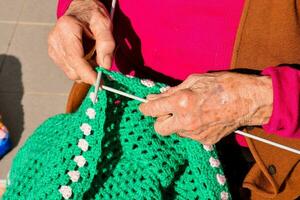 ett äldre kvinna är stickning en färgrik virka filt foto