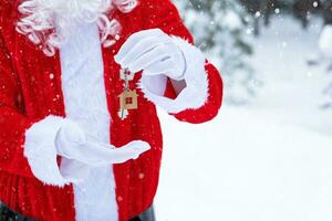 husnyckel med nyckelring stuga i händerna på jultomten utomhus i snö. affär för fastigheter, köp, konstruktion, flytt, inteckning. mysigt hem. god jul, nyårsbokningsevenemang och hall foto