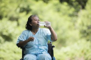 gammal kvinna sitter på rullstol med vattenflaska efter att ha tagit ett läkemedel foto
