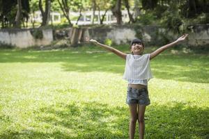 glad liten flicka visar upp handen i luften i trädgården foto