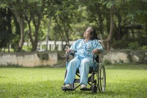 ensam äldre kvinna som sitter på rullstol i trädgården på sjukhuset