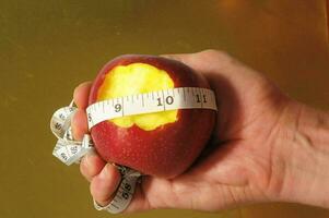 en person innehav ett äpple med en mätning tejp runt om den foto