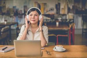 glad asiatisk kvinna som kopplar av och lyssnar på musik i kaféet foto