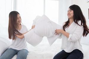 två asiatiska tjejer gör kuddkamp i sovrummet som barndom foto