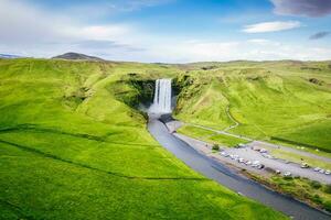 skogafoss vattenfall strömmande från klippa omgiven förbi frodig landskap i sommar foto