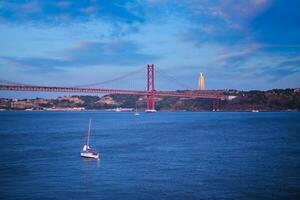 se av 25 de abril bro över tagus flod, christ de kung monument och en Yacht båt i de kväll. Lissabon, portugal foto