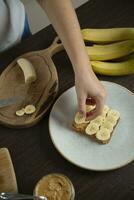jordnöt Smör smörgås med banan - kvinna framställning frukost. foto