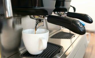 de kaffe maskin häller kaffe in i en kopp. framställning aromatisk naturlig kaffe. närbild. selektiv fokus. foto