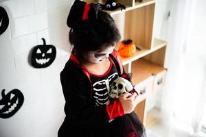 porträtt asiatisk liten flicka i halloweenkostym som håller skallen foto