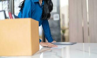 företag kvinna sändning avgång brev och förpackning grejer avgå sänka eller bärande företag kartong låda förbi skrivbord i kontor. förändra av jobb eller sparken från företag foto