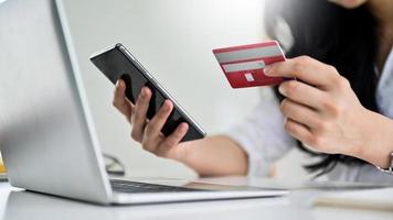 ung kvinna som håller kreditkort och smartphone med bärbar dator, foto