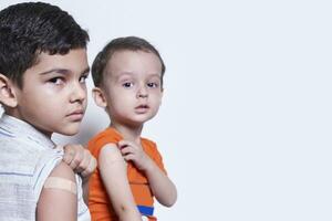 två Pojkar som visar deras ärm med lim bandage plåster efter vaccination. injektion covid vaccin, immunisering för familj foto