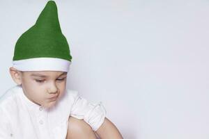 en liten unge framställning en rolig irriterad ansikte. irriterad jul pojke i santa hatt. en verkligen allvarlig och stilig unge foto