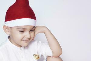 en liten unge framställning en rolig irriterad ansikte. irriterad jul pojke i santa hatt. en verkligen allvarlig och stilig unge foto