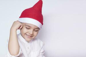 porträtt av leende blyg pojke. sexåring unge blyg och leende. fira jul. 6-7 år gammal barn med santa hatt. foto