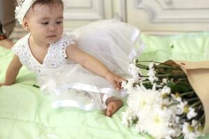 bebis flicka i vit klänning spela med bukett av blommor foto