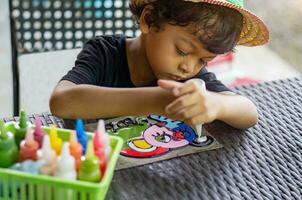 asiatisk pojke är spelar med plast Färg måla på zink ark. foto